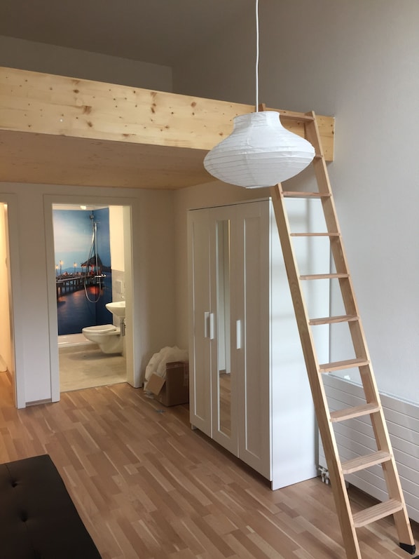 A room with a wooden floor, a white wardrobe, a wooden ladder, and a hanging light fixture. - Hostel Airport Oberglatt (Oberglatt)