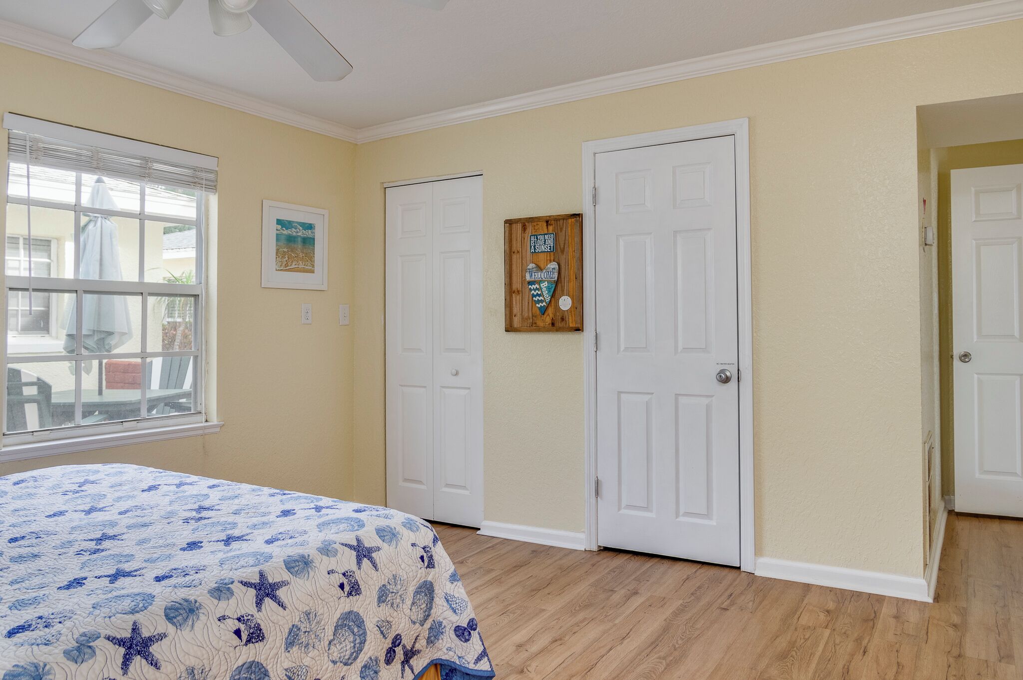 Un dormitorio con una cama, dos puertas blancas, una ventana con persianas y un cuadro en la pared.