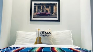 Un dormitorio con cama, almohadas, un cuadro enmarcado en la pared y luces empotradas en el techo.