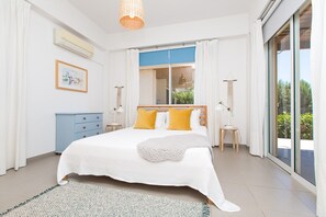 A bedroom with a bed, a dresser, a window, and a view of greenery.