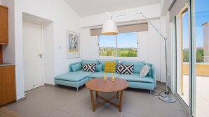 Un salon moderne avec un canapé de couleur turquoise, une table basse en bois et une grande fenêtre donnant sur un paysage verdoyant.