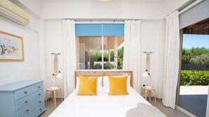 Une chambre à coucher avec un grand lit, deux lampes de chevet, une fenêtre à cadre bleu et une vue sur la verdure.