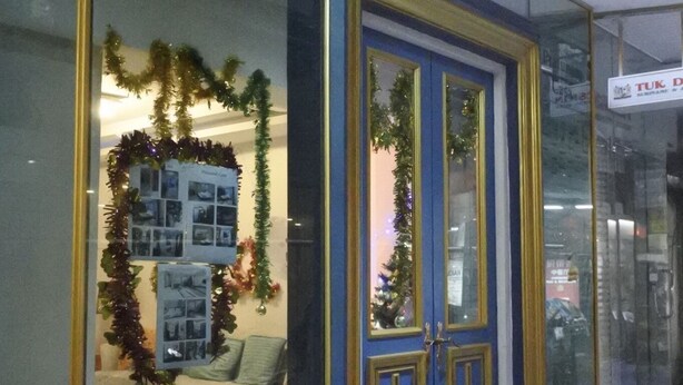 A storefront with a blue and gold door, a Christmas wreath, and a display of framed photos. - Pratunam Casa (Bangkok)