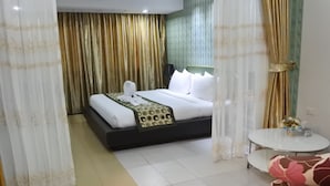 A hotel room with a bed, curtains, a small round table with a vase, and a chair. - Pratunam Casa (Bangkok)