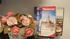 A magazine stand with a 'Thailand' travel guide and a vase of pink roses. - Pratunam Casa (Bangkok)