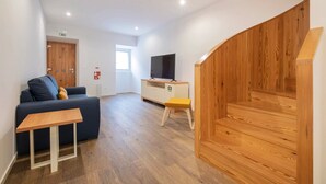 A modern living room with a sofa, a small wooden table, a TV on a cabinet, and a wooden staircase.