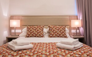 Una cama bien hecha con un edredón estampado con motivos geométricos, dos almohadas a juego y dos lámparas de noche.