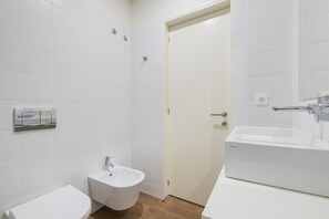 Un baño con azulejos blancos, un bidé, un inodoro y un lavabo.