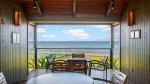 Un balcón con vista a la playa, paredes de madera y una mesa redonda con sillas.