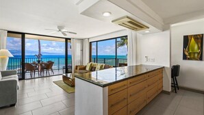 Una cocina moderna con una isla grande, un comedor con vistas al océano y un ventilador de techo.