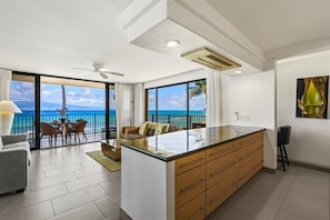A modern kitchen with a large island, a dining area with a view of the ocean, and a ceiling fan.