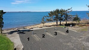 Un espace de stationnement avec des places numérotées de 1 à 4, une plage de sable et une étendue d’eau en arrière-plan.