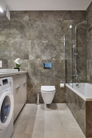 Een moderne badkamer met een wasmachine, toilet en bad.