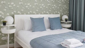 Een slaapkamer met een wit bed, blauw beddengoed en bloemenbehang.
