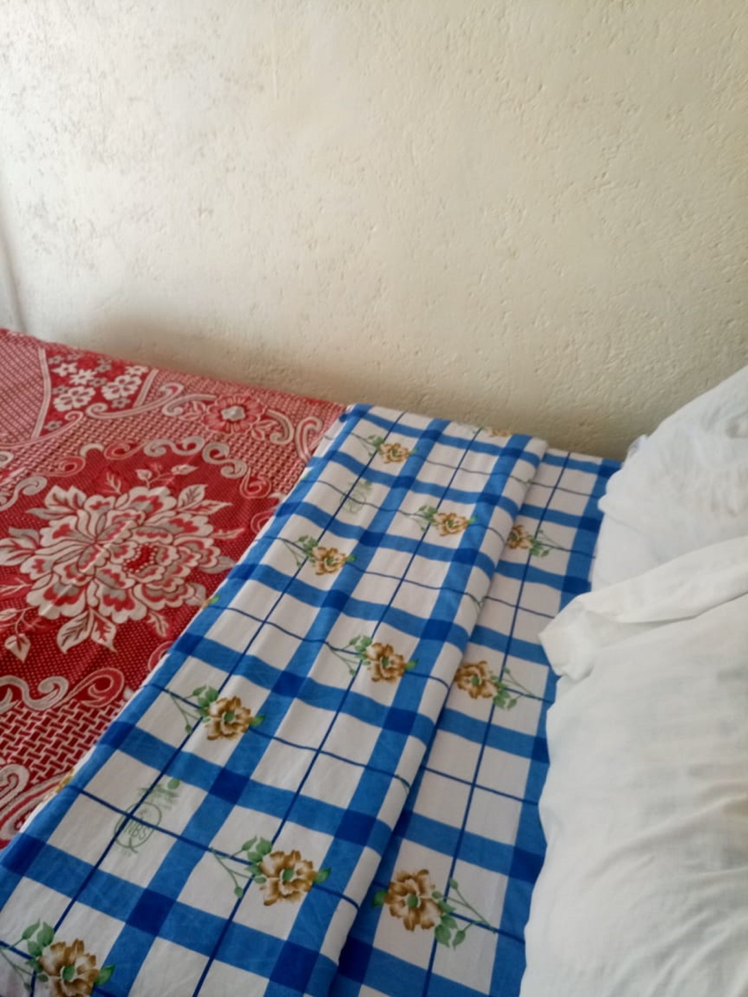 Una cama con una colcha azul y blanca a cuadros y otra colcha con estampado floral rojo.