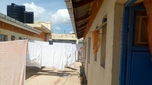 A narrow outdoor corridor with a blue door on the right, a concrete floor, and white cloths hanging on the left.