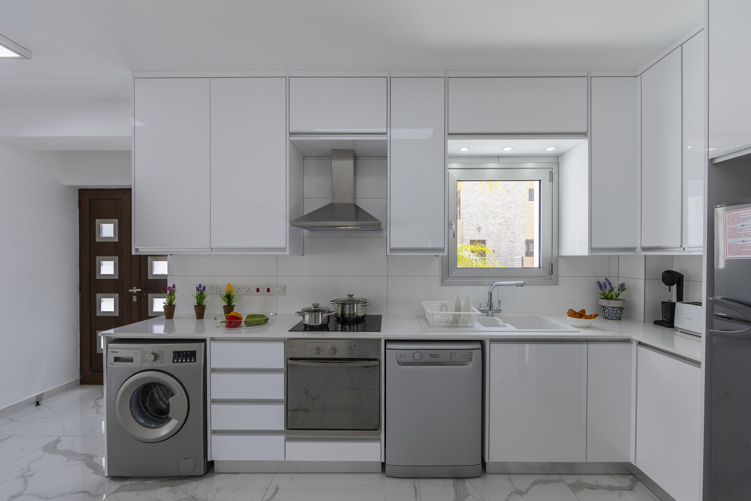 A modern kitchen with built-in appliances, a window, and a door with a view.