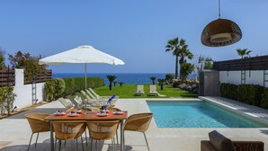 An outdoor dining area with a view of the ocean, a pool, and lounge chairs. - Protaras Beachfront Villa Pietra (Protaras)