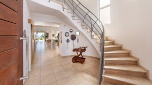 A spacious interior with a wooden staircase, a dining area, and a wall decorated with clocks and wall art. - Protaras Beachfront Villa Pietra (Protaras)