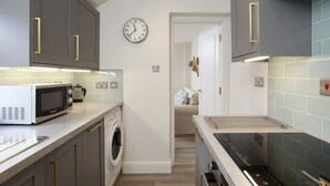 Une cuisine moderne avec des meubles gris, un four à micro-ondes, un lave-linge et une horloge au mur.