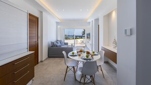 A modern dining area with a round table, white chairs, and a view of the outdoors. - Mackenzie Castella Beachfront Suite (Larnaca)