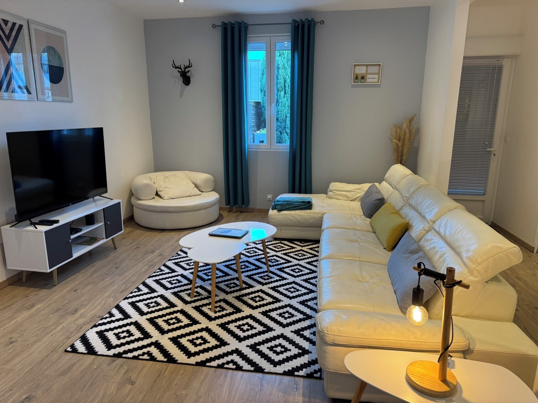 A modern living room with a flat-screen TV, a round white sofa, a beige sofa, a coffee table, and a patterned rug.
