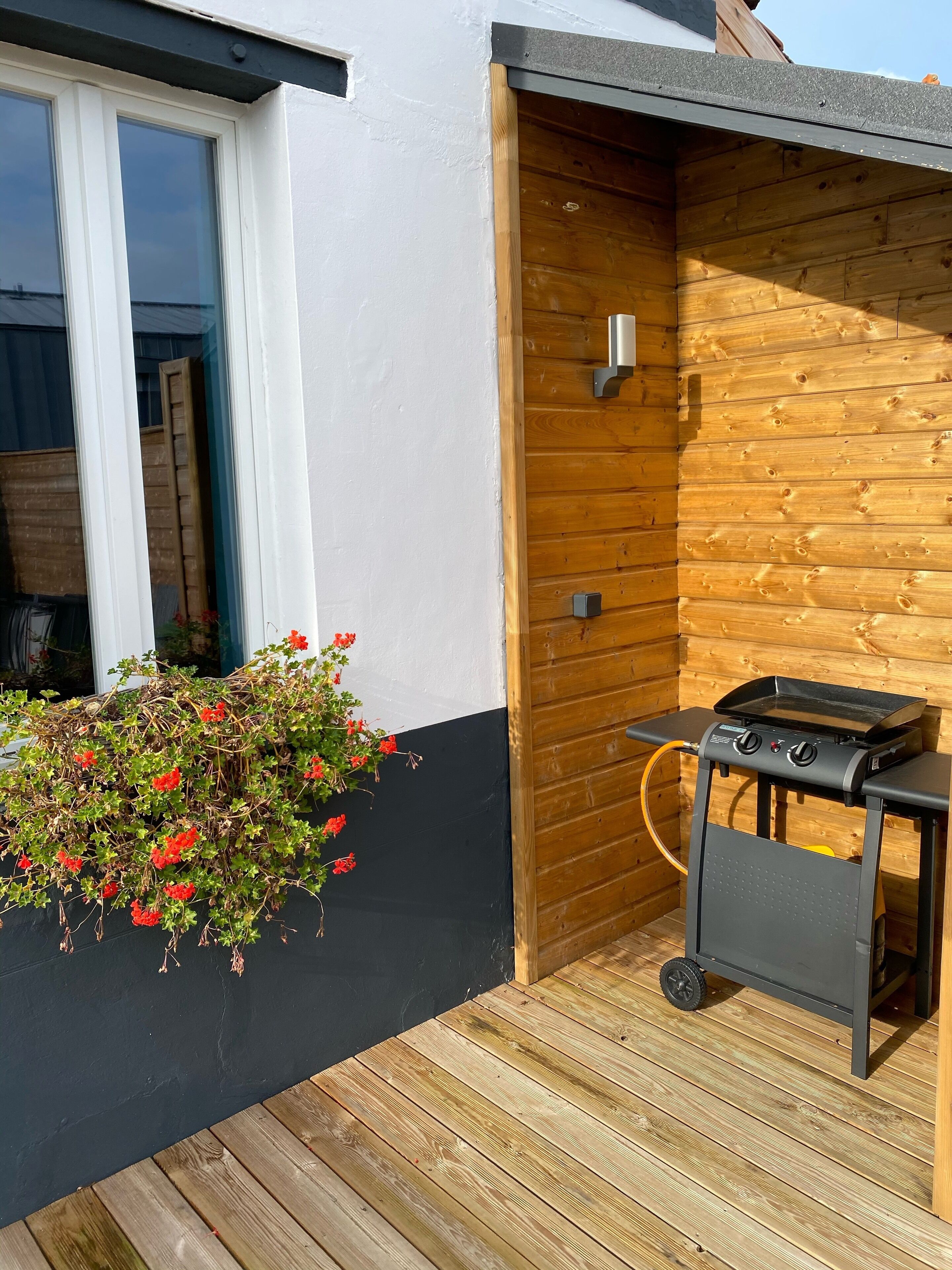 A wooden deck with a barbecue grill and a planter with red flowers.
