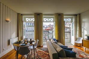 A dining area with a table set for breakfast, a sofa, and a view of buildings through large windows. - Loft exclusive to Clérigos (Porto)