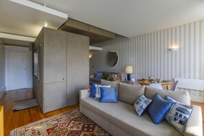 A modern living room with a sofa, pillows, a rug, and a dining area with a table and chairs.