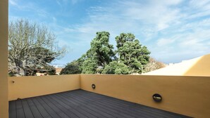 Une terrasse sur le toit, dotée d’un plancher en bois, de murs jaunes et offrant une vue sur les arbres et les bâtiments.