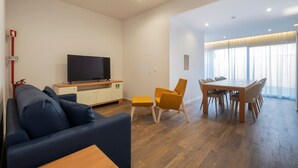 Un salon moderne comprenant un canapé, un téléviseur, une table à manger avec des chaises et une petite table avec une chaise.