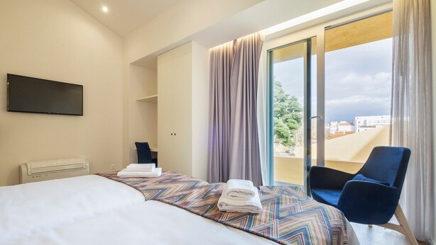 Une chambre d’hôtel avec un lit, une chaise, une télévision et une vue sur la ville.