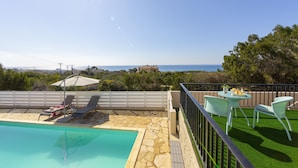 Ein Pool mit Liegestühlen und einem Tisch, Meerblick und ein Balkon mit Sitzgelegenheiten.