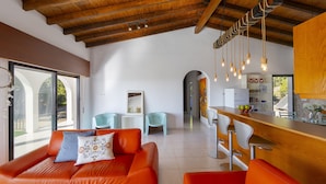 Ein modernes Interieur mit Holzbalkendecke, orangefarbenen Sofas, einer Küchenzeile und einem Essbereich.