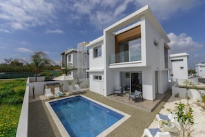 Una casa moderna de dos pisos con piscina, mobiliario exterior y jardín.