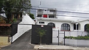 A gated entrance with a black gate, a small tree, and a white building with arched windows in the background.