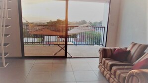 A living room with a sofa, a dining table with chairs, and a view of a balcony with a hammock.