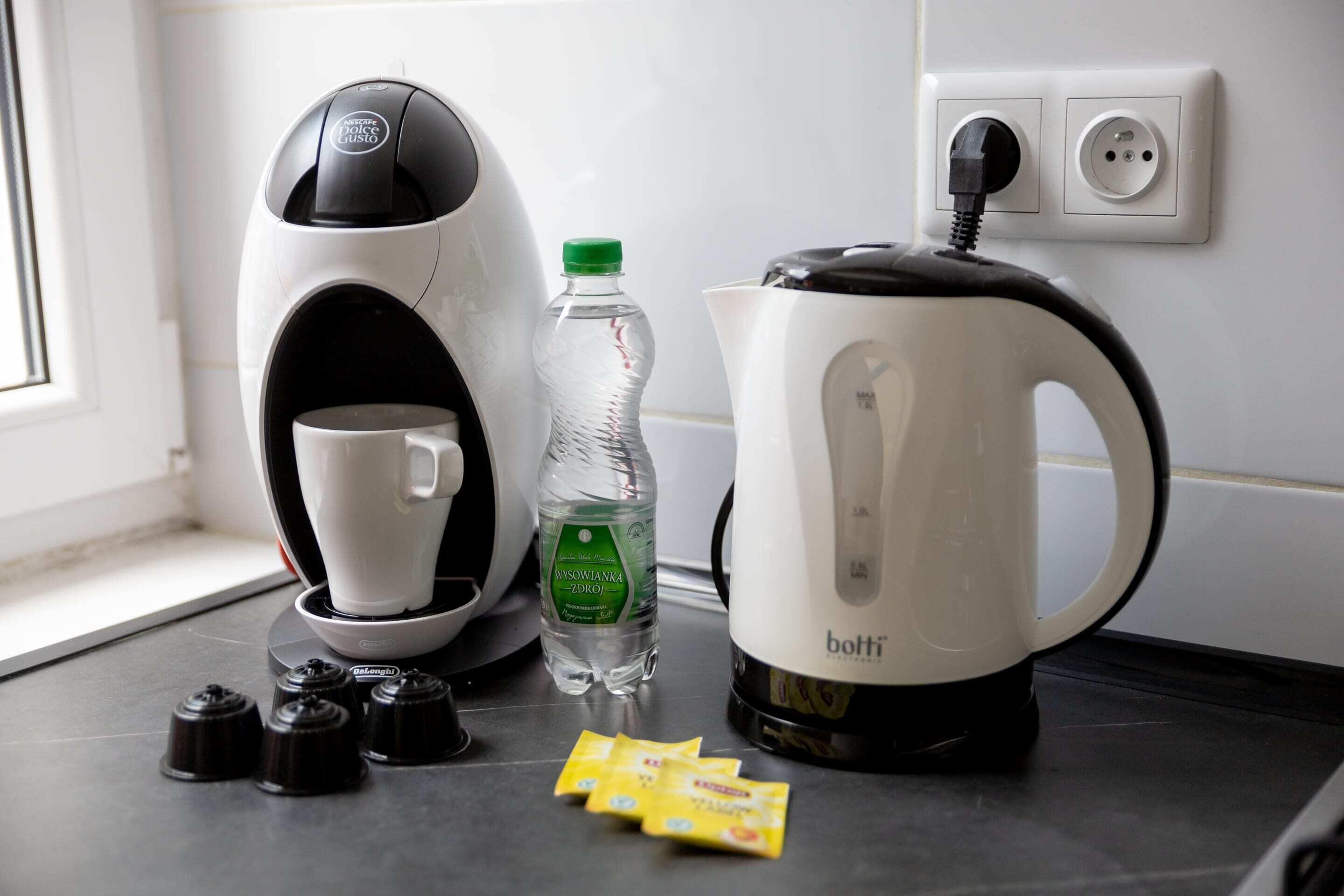 A coffee machine, a water bottle, a kettle, and coffee pods on a kitchen counter.