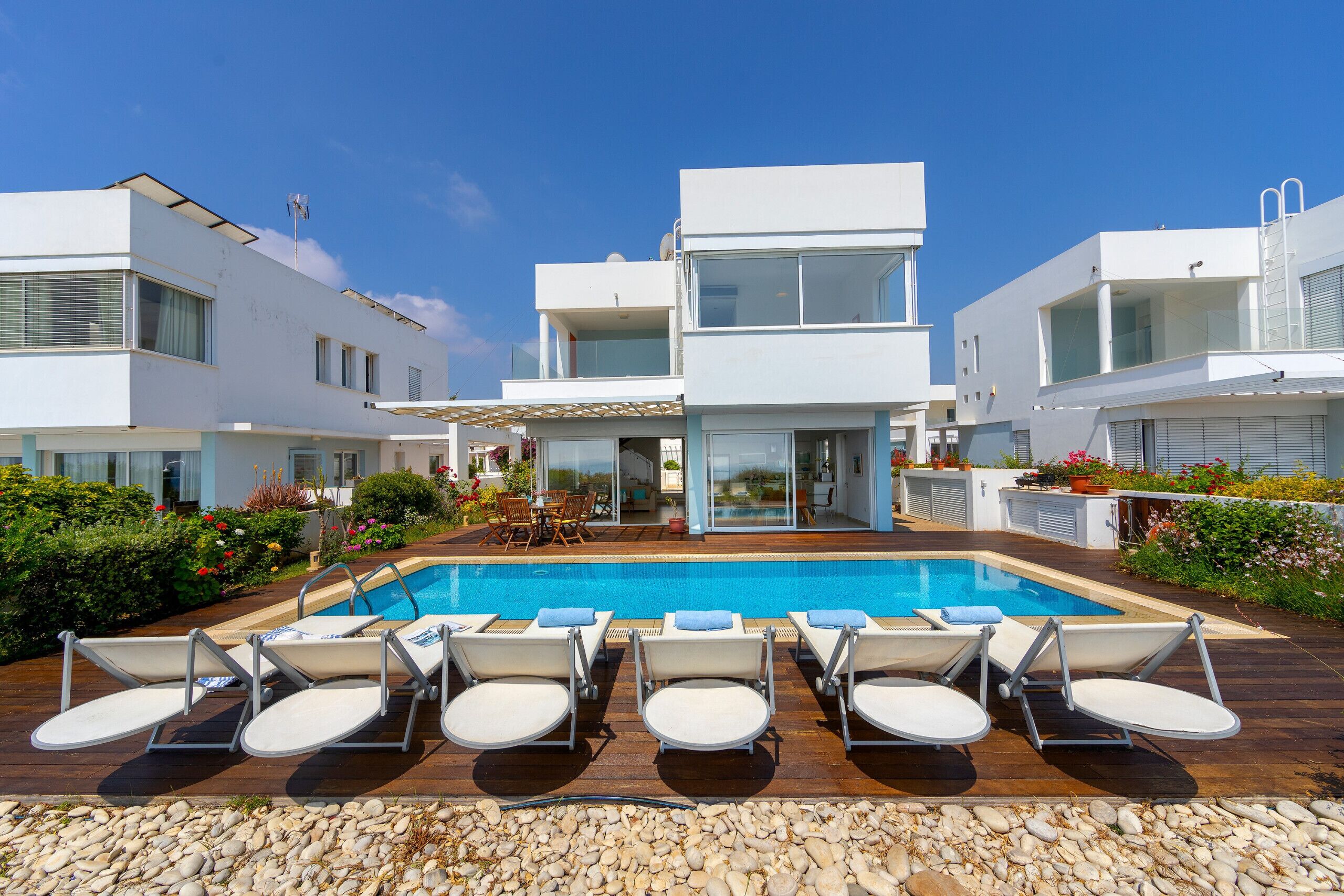 Une villa moderne dotée d’une piscine, de plusieurs chaises longues et d’un jardin bien entretenu.