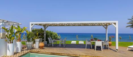 A poolside area with a pergola, outdoor seating, and a view of the ocean.