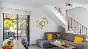 A modern living room with a grey sofa, yellow cushions, a wooden coffee table, and a staircase. - Protaras Villa Angela Nefeli (Protaras)