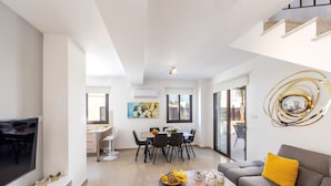 A modern living room with a flat-screen TV, a sofa with a yellow pillow, and a dining area with a table and chairs. - Protaras Villa Angela Nefeli (Protaras)