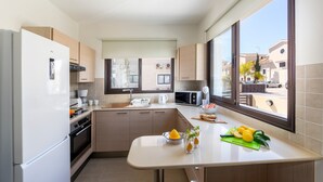 A modern kitchen with a built-in oven, microwave, and a large window offering a view of the street. - Protaras Villa Angela Nefeli (Protaras)