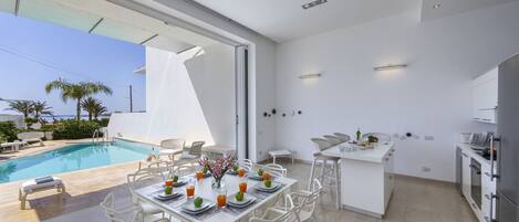 Een moderne keuken met witte kasten en een eethoek met uitzicht op een zwembad.