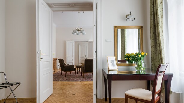 A room with a wooden floor, a desk with a mirror, a chair, and a vase with flowers. - KrakowRentals - Belle Epoque 2 Apartment (Kraków)