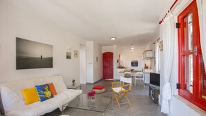 A modern living room with a sofa, a glass coffee table, and a dining area with a white chair and table. - Protaras Liora Seaview Suite (Protaras)