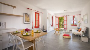 A modern kitchen with white appliances, a dining area with a wooden table and chairs, and a living area with a sofa and a red cushion. - Protaras Liora Seaview Suite (Protaras)