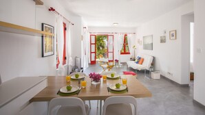 A modern dining area with a wooden table set for two, a sofa, and a view of the outdoors. - Protaras Liora Seaview Suite (Protaras)