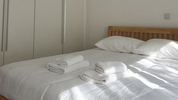 A bedroom with a bed, white towels, a wooden headboard, and a wardrobe. - Villa Imogine with Sea View (Neo Chorio)