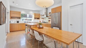 A modern kitchen with wooden cabinets, a stainless steel refrigerator, and a wooden dining table with chairs. - The Local - 2 Blocks to Downtown Fay (Fayetteville)